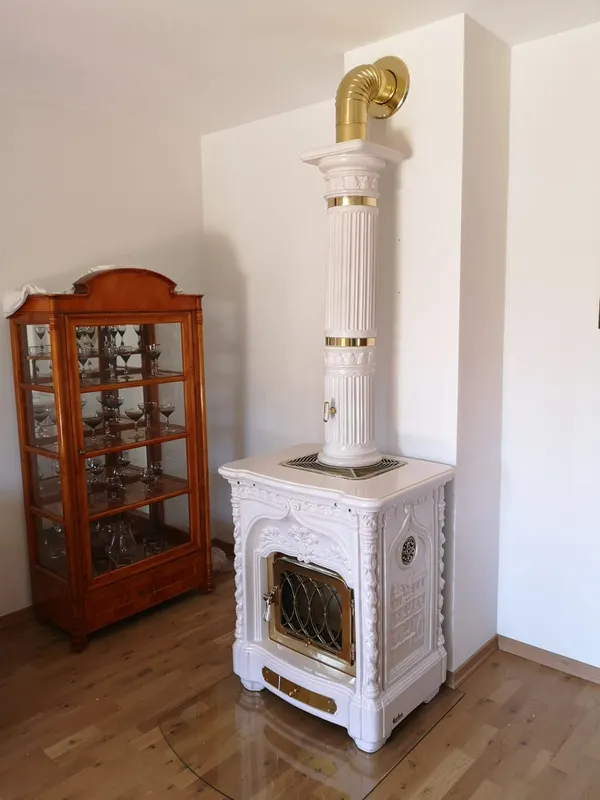 Weißer Keramikofen mit goldfarbenen Details und Rauchrohr